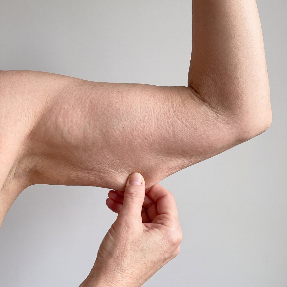 Close-up of loose skin under the arm, pinched between two fingers